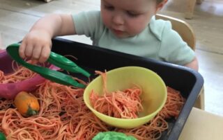 Nursery child using pinchers to grab spaghetti
